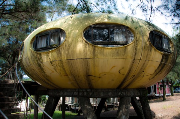A rusted yellow spherical building sits on four legs.